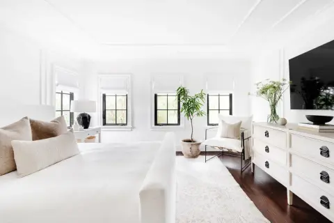 A serene, feminine black and white bedroom with a plush white bed, textured pillows, and a black lamp.