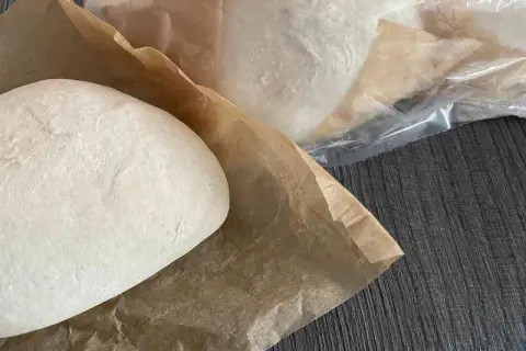 Frische Pizzaböden, bereit für das Pizzateig einfrieren. Einer liegt auf Backpapier, weitere sind in Folie verpackt.
