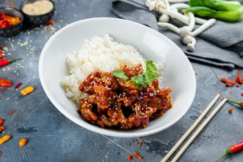 Pyszny kurczak bac bo w sosie z sezamem, podany z ryżem. Obok pałeczki i papryczki chili.