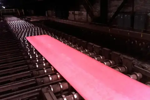Gorący, różowy metal przesuwa się po rolkach w hucie, będąc częścią cyklu produkcyjnego.