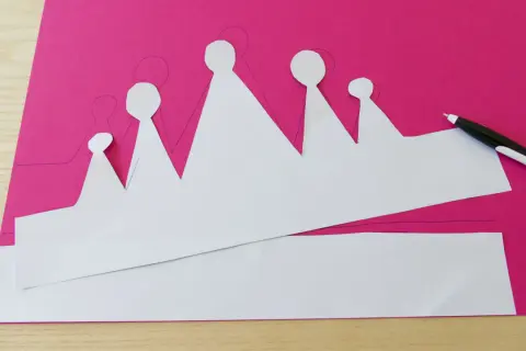 Sagoma di una corona da colorare su carta fucsia, pronta per essere ritagliata e decorata.