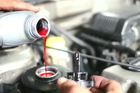 Main d'un mécanicien versant du liquide de frein rouge vif dans le réservoir d'un véhicule.
