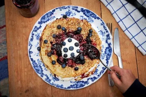 En hög med pannkakor toppas med grädde, blåbär och en generös klick drottningsylt. Perfekt för ett mysigt fika.