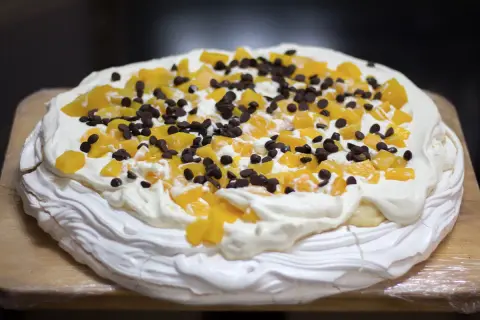 En härlig anna pavlova tårta med vispgrädde, persikobitar och chokladknappar.