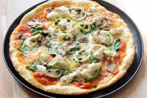 Pyszna pizza z kurczakiem, pieczarkami i szpinakiem, polana sosem pomidorowym.