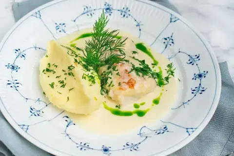 En vacker tallrik med torskrygg recept, serverad med krämigt potatismos och en grön dillolja.