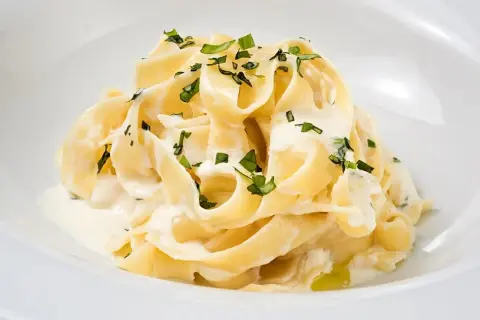Kremowy makaron tagliatelle z sosem mascarpone i posiekaną natką pietruszki.