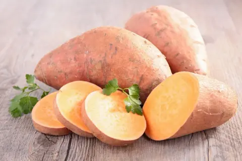 Patates douces entières et tranchées, garnies de persil frais, sur fond de bois. Un délice orangé prêt à être cuisiné.