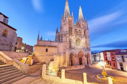 Majestuosa catedral de Burgos al anochecer, con sus agujas góticas iluminadas y el cielo azul crepuscular.
