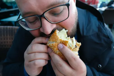Mężczyzna w okularach je dużego burgera.