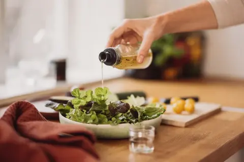 Frische Salatblätter werden mit einem Dressing beträufelt. Rotweinessig ist eine gesunde Wahl, besonders in der Schwangerschaft.