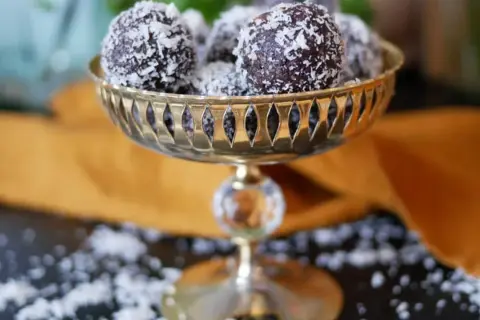 Nyttiga chokladbollar rullade i kokosflingor, serverade i en vacker guldfärgad skål. En perfekt, hälsosam godsak!