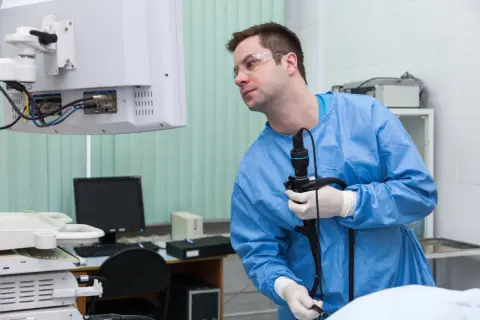 Lekarz w niebieskim fartuchu i okularach ochronnych trzyma endoskop, przygotowując się do badania. Czy gastroskopia boli? Procedura jest zazwyczaj bezbolesna.