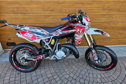 Husqvarna TE 125 z agresywnym oklejeniem w czerwono-białe wzory, gotowa do jazdy po torze.