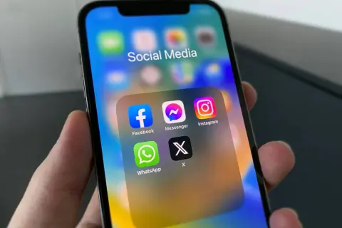 Na ekranie iPhone'a widać folder "Social Media" z ikonami Facebook, Messenger, Instagram, WhatsApp i X. Dowiedz się, jak włączyć powiadomienia Messenger.