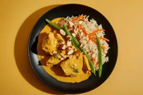 Pyszny kurczak curry w kremowym sosie, podany z ryżem, fasolką szparagową i migdałami.