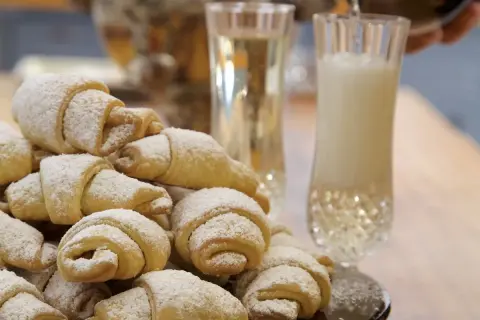 Stos rogalików krucho-drożdżowych z 1 kg mąki, posypanych cukrem pudrem, obok kieliszków z napojem.