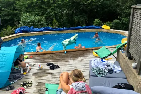 Barn njuter av en solig dag vid poolen, med en uppblåsbar haj och flytleksaker. En bebis leker i ett tält på altanen, perfekt för spf barn.