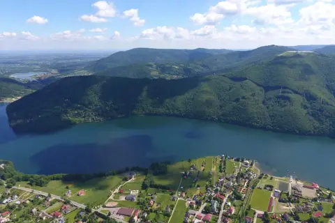 Malownicze krajobrazy i jezioro w Międzybrodziu Bialskim. Widać zabudowania, pola i zalesione wzgórza, idealne na wypoczynek i odkrywanie atrakcji.