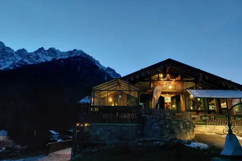 Rifugio alpino illuminato con una stella di Natale, circondato da montagne innevate. I forni di sopra sono spenti, ma l'atmosfera è calda e accogliente.