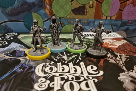Cztery figurki postaci z gry planszowej "Cobble & Fog" na tle planszy. Atmosfera unmatched bruk i mgła.