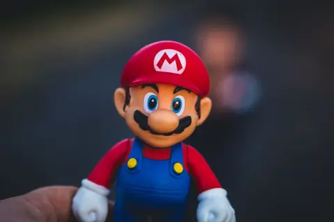 Figurka Mario w czerwonej czapce z literą M i niebieskich ogrodniczkach, trzymana na dłoni.