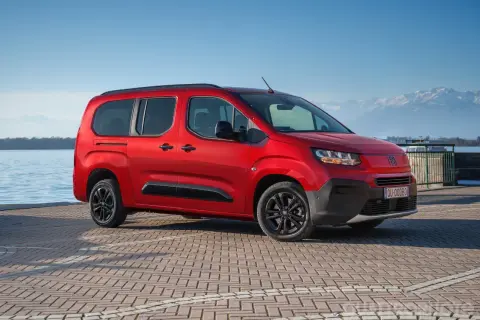 Fiat Qubo rosso fiammante parcheggiato sul lungolago, con montagne innevate sullo sfondo. Le diverse fiat qubo motorizzazioni offrono versatilità.