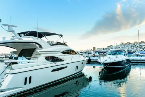 Luksusowe jachty cumują w słonecznym Puerto Banús. Błękitne niebo i spokojna woda odbijają białe kadłuby.