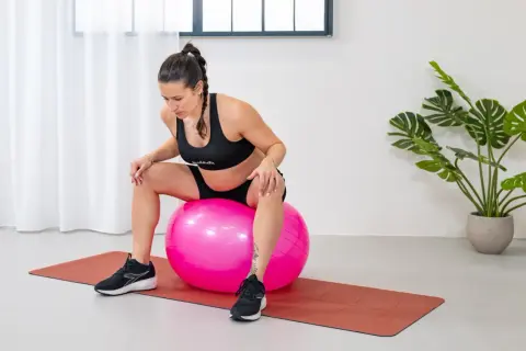 Mujer embarazada sentada en una pelota de ejercicio rosa, preparándose para fortalecer el suelo pélvico.