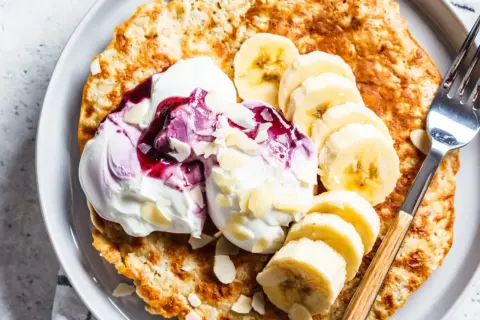 Puszysty omlet z bananem, udekorowany bitą śmietaną, musem jagodowym i płatkami migdałów. Idealne śniadanie.