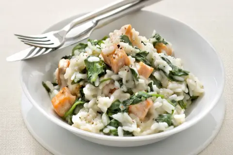 Un crémeux risotto épinard avec des morceaux de saumon. Un plat savoureux et coloré, prêt à être dégusté avec une fourchette et un couteau.