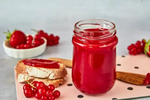 Glas mit Erdbeer Johannisbeer Marmelade, daneben Brot mit Marmelade und frische Beeren.