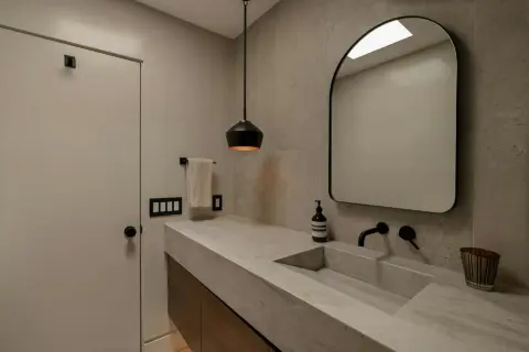 Élégante salle de bain avec un lavabo en **béton ciré** intégré, un miroir arqué et un éclairage moderne.