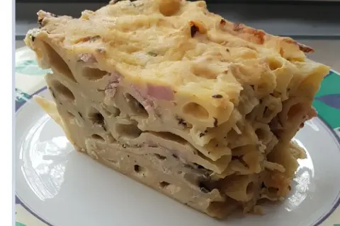 Kawałek zapiekanki makaronowej z serem i szynką na talerzu.