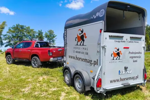 Czerwony pickup holuje przyczepę do przewozu koni. Na przyczepie logo Horse-Mag i napis "Uwaga Konie".