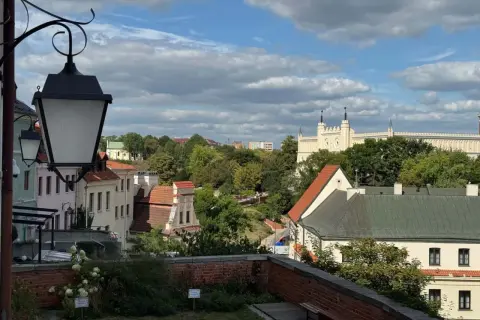 Widok na Lublin na weekend. Zabytkowe kamienice, zieleń i biały zamek na wzgórzu pod błękitnym niebem.
