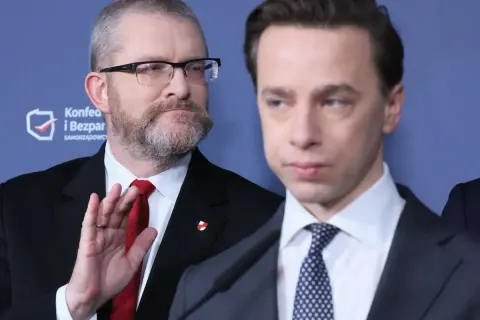Dwóch mężczyzn w garniturach, jeden z brodą i okularami, drugi z wyrazem twarzy.