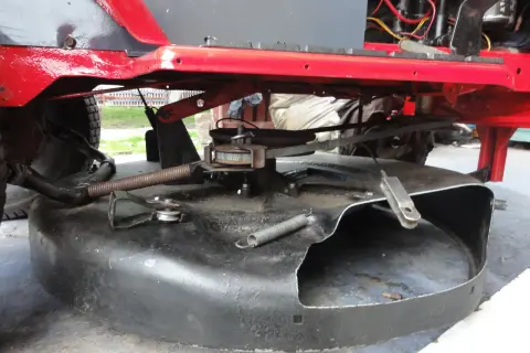 Podczas naprawy traktorka, widać mechanizm kosiska z pasem napędowym i sprężyną.