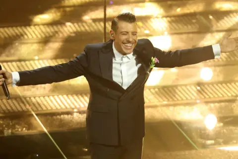 Un artista sorridente sul palco di Sanremo, con microfono in mano, pronto per i duetti.