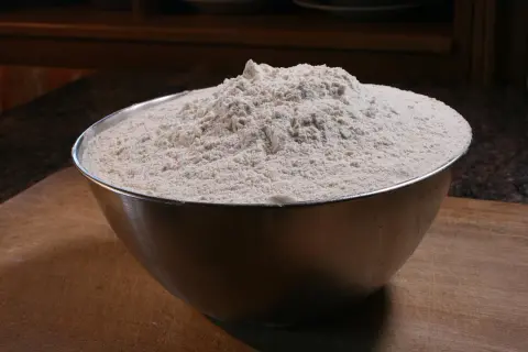 Miska pełna mąki na desce do krojenia.