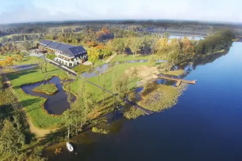 Malownicze miejscowości na Mazurach: hotel nad jeziorem, otoczony zielenią i jesiennymi drzewami. Drewniane pomosty zapraszają do wodnych przygód.