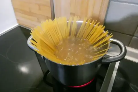 Długie spaghettoni gotują się w garnku na kuchence.