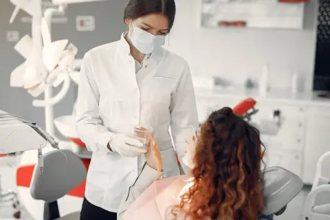 Dentystka w masce podaje wodę pacjentce. Bezpieczne leczenie kanałowe w ciąży jest możliwe.