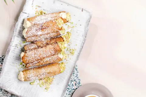 En bricka med flera italienska bakelser, cannolis, pudrade med florsocker och garnerade med hackade pistagenötter.