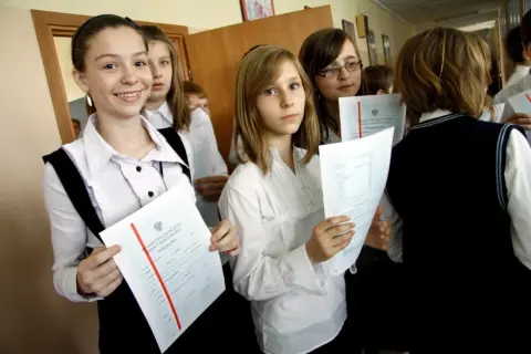 Uczennice z dumą trzymają świadectwa ukończenia szkoły. Na jednym z nich widoczny jest czerwony pasek średnia.