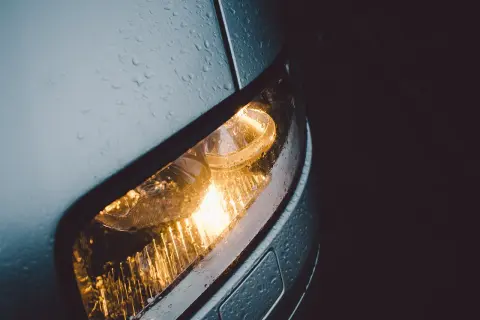 Światła postojowe samochodu świecą w deszczu. Krople wody na karoserii i kloszu lampy tworzą ciekawy efekt.