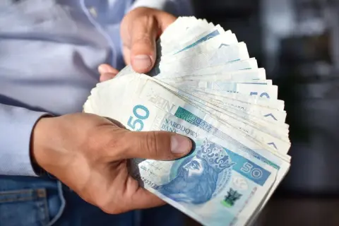 Dłonie trzymają stos banknotów 50 zł. Czy to już kwota netto?