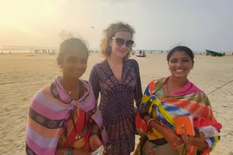 Trzy kobiety na plaży w Indiach. Jedna z nich trzyma pomarańczowy notes, może to notatnik do zapisywania cen rupii, czyli waluty w Indiach.