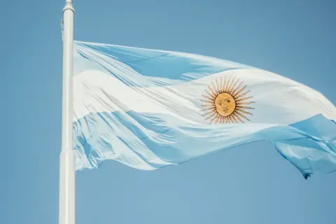 Flaga Argentyny powiewa na wietrze na tle błękitnego nieba.