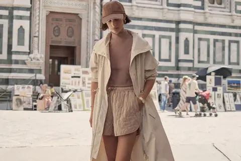 Frau im Athleisure Style mit beiger Jacke und gesteppten Shorts vor einer historischen Fassade.